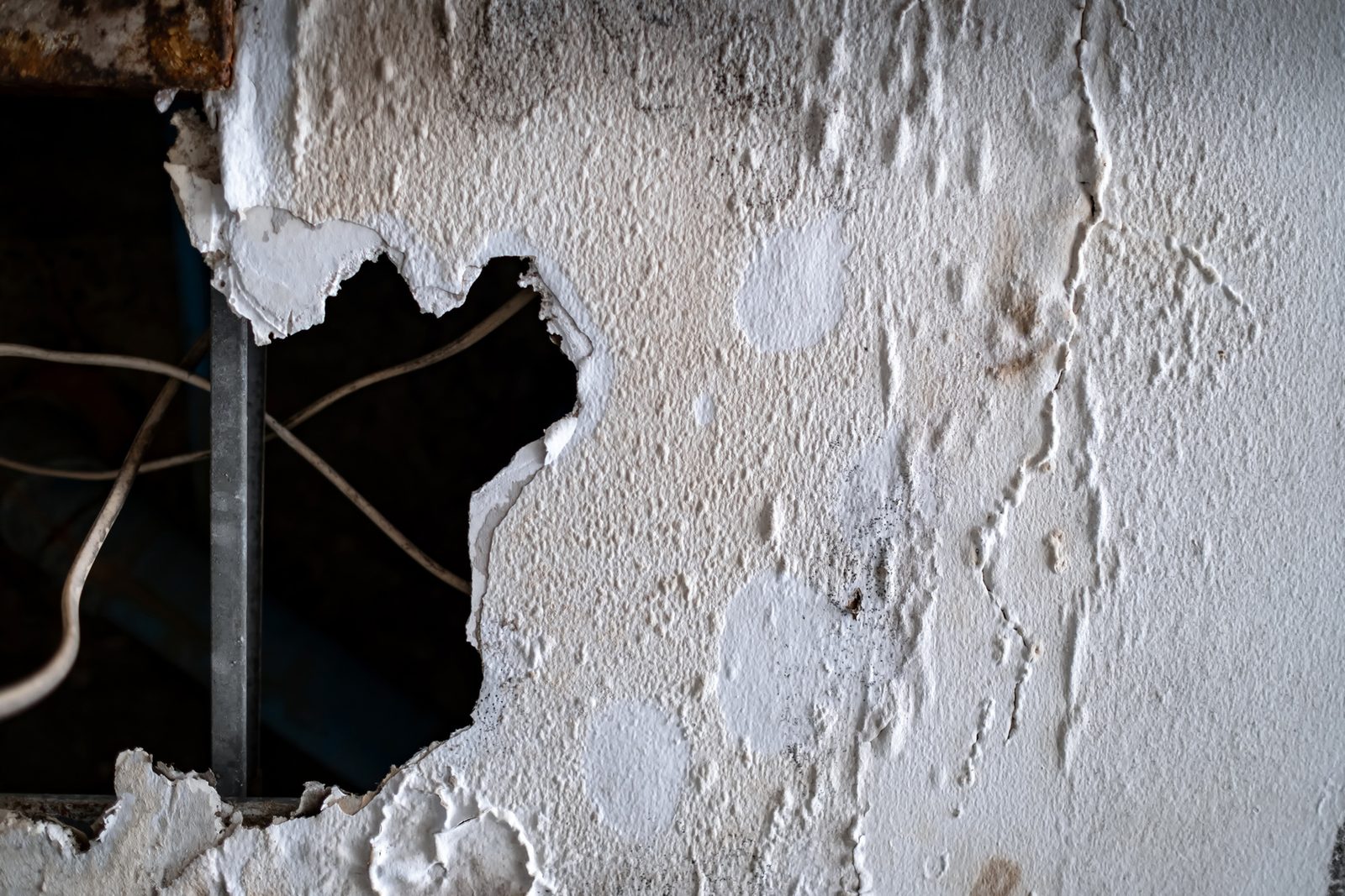 Large hole in a water-damaged wall with peeling plaster